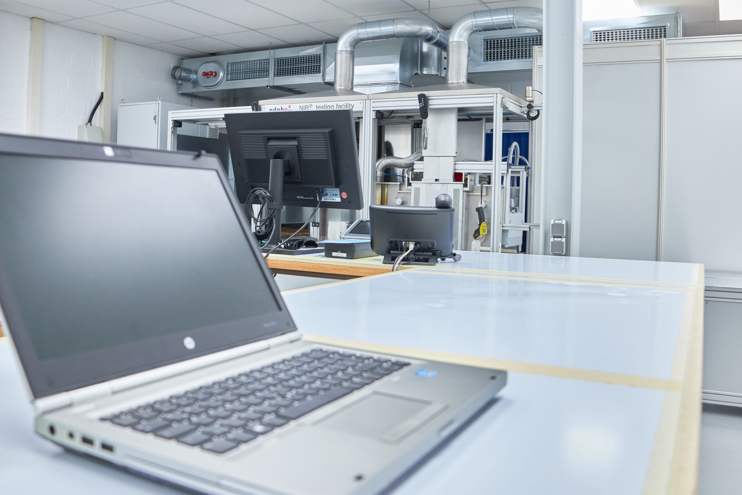 Laborraum mit Laptop: zu sehen ist das application Lab der Firma adphos mit Fokus auf einen Laptop im Vordergrund links unten im Bild